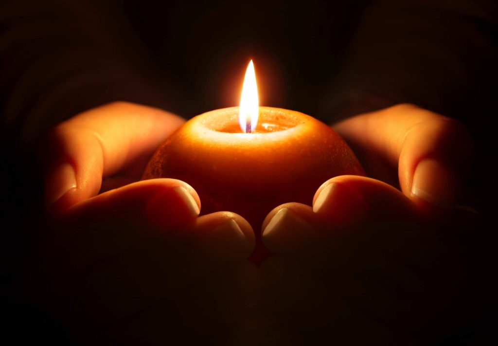 Burning candle held in two hands